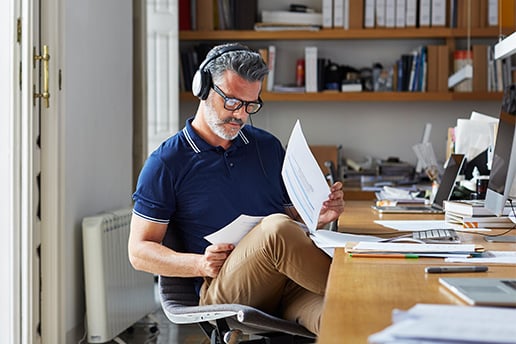 Man wearing headphones and glasses, sitting at his desk and sorting through documents