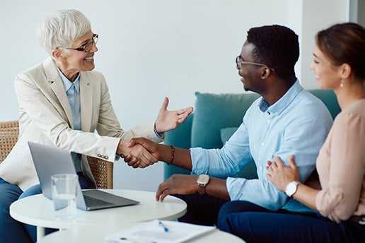 Older woman happily shaking hands with a young couple while they all sit together in an office