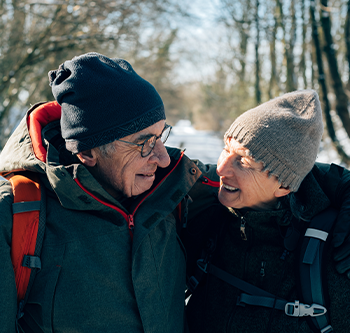 An elderly couple bundled up taking a walk in the snow