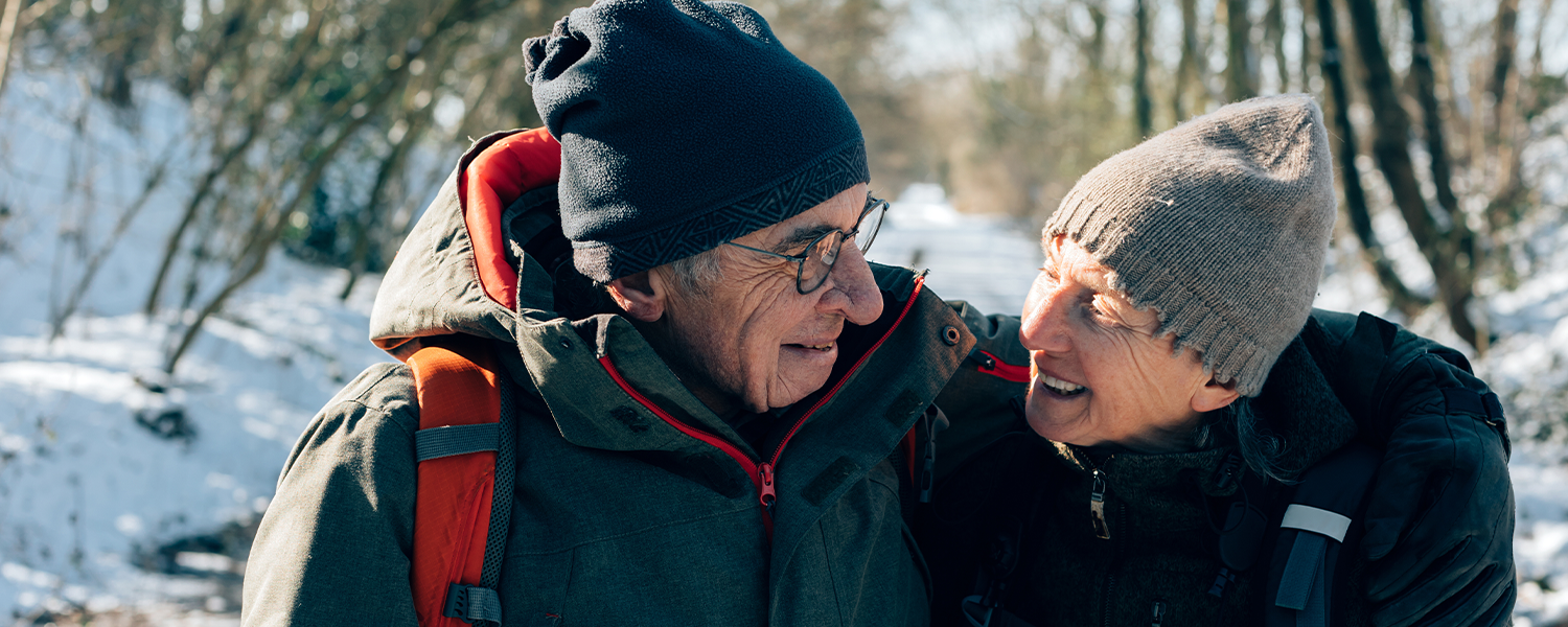 An elderly couple bundled up taking a walk in the snow