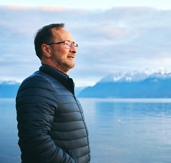 Man standing near a lake with mountains behind him looking off into the distance