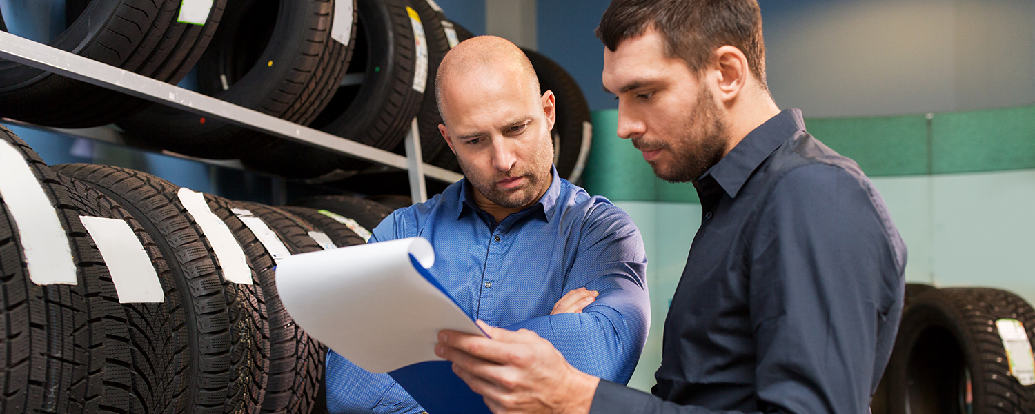 Two men looking at a clipboard standing next to a row of tires