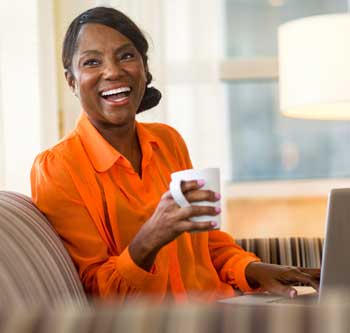 Woman in orange shirt holding coffee and laughing